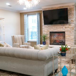 A modern living room with a comfortable sofa, stone fireplace, and a mounted television under an elegant chandelier.