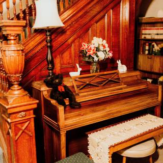 A cozy corner featuring a vintage wooden piano next to a staircase, adorned with decorative items and books.