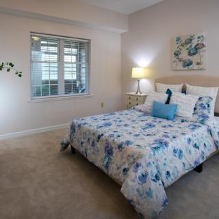 A cozy bedroom with floral bedding, a bedside lamp, and a window letting in natural light.
