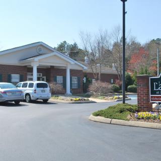 A small brick building with a parking lot and cars in front, surrounded by trees.