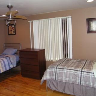 A cozy bedroom with two twin beds, a wooden dresser, and large window blinds.