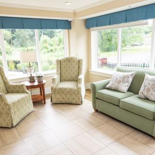 A cozy living room featuring a green sofa, patterned chairs, and large windows letting in natural light.