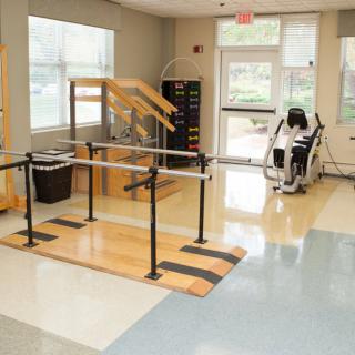 A rehabilitation room equipped with parallel bars, exercise equipment, and therapy stairs.