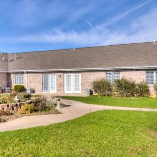 A single-story brick house with a well-maintained lawn and garden on a sunny day.