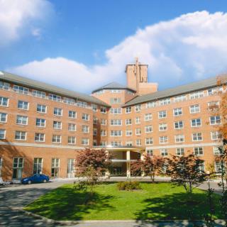 A large brick hospital building with a clear blue sky and scattered clouds in the background.