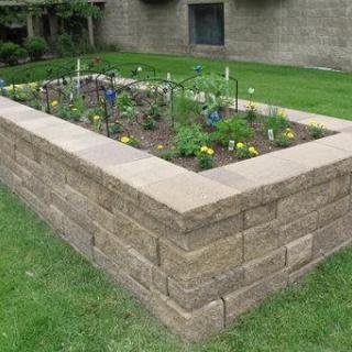 A raised garden bed constructed with stone walls, featuring various plants and vegetables.