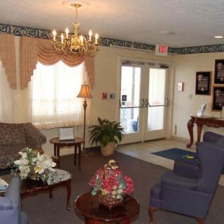A cozy living room with elegant furnishings, featuring a chandelier, couches, armchairs, and decorative plants.