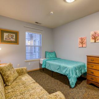 A cozy bedroom featuring a single bed with teal bedding, a wooden dresser, and a comfortable sofa.