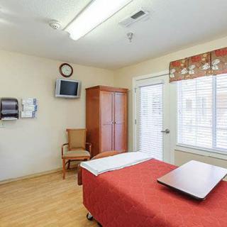 A clean and quiet hospital room with a bed, television, chair, and wardrobe.