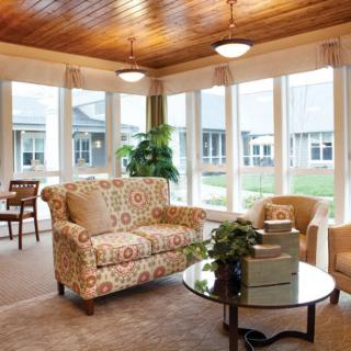 A cozy living room with ample natural light, featuring a patterned sofa and comfortable chairs around a glass table.