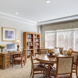 A well-lit office space with a desk, bookshelf, and round table with chairs.