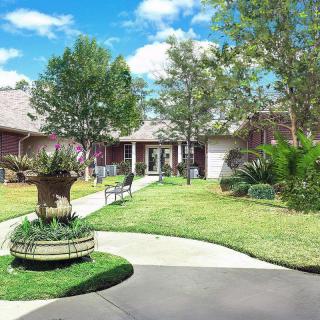 A scenic outdoor garden with a pathway, bench, and surrounding trees leading to a building.