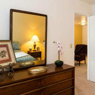 A cozy bedroom featuring a wooden dresser with a mirror and decorative items.