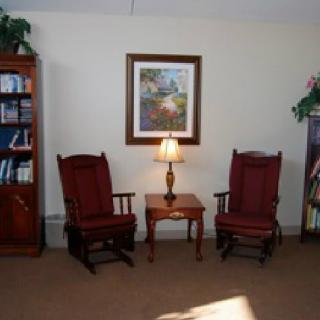 A cozy living room with two rocking chairs, a small table with a lamp, and bookshelves.