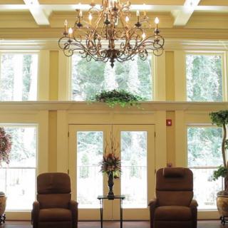 A spacious, well-lit lobby with large windows, ornate chandelier, and comfortable seating.