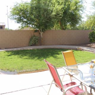 A sunny backyard with a patio, lawn, and outdoor seating.