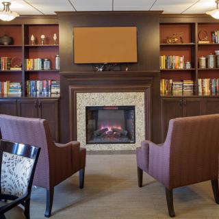 A cozy library setting with a fireplace, surrounded by bookshelves and comfortable armchairs.