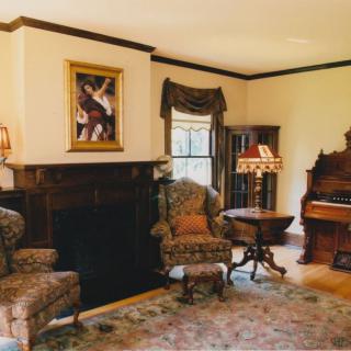 A cozy vintage-style living room featuring a fireplace, patterned armchairs, and an antique organ.