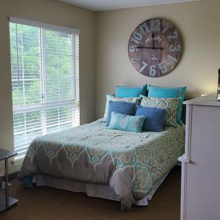 A cozy bedroom featuring a neatly made bed with decorative pillows and a large wall clock.