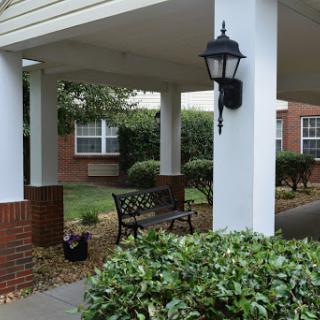 A cozy outdoor seating area with a bench and decorative lantern, surrounded by lush greenery.