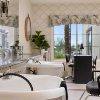 A bright and stylish salon interior featuring hair washing stations, chairs, and large mirrors by a window.