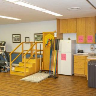 A rehabilitation room equipped with exercise stairs, a kitchen setup, and various therapy tools.