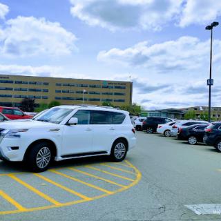 A white SUV parked in a spacious parking lot under a cloudy sky, with a building in the background.