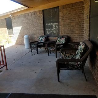 A cozy outdoor seating area featuring wicker chairs with decorative cushions, set against a brick wall.
