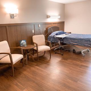 A serene hospital patient room featuring a bed, two chairs, and warm lighting.