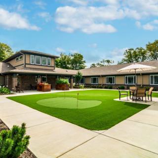 A modern residential house with a spacious yard featuring a putting green and outdoor seating area.