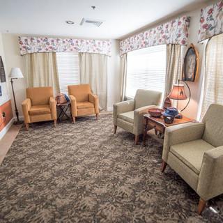 A cozy living room setup with several armchairs, a patterned carpet, and large windows with curtains.