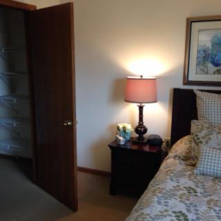 A cozy bedroom with a bed, nightstand, and lamp near an open door.