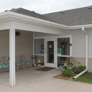 An exterior view of a building entrance with an overhang and chairs.