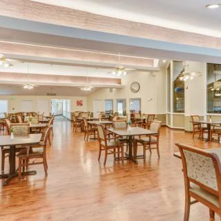 Spacious dining area with wooden tables and chairs, featuring a polished wood floor and soft lighting.