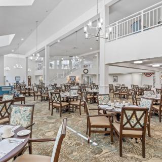 A spacious and bright dining room with neatly arranged tables and chairs, featuring elegant chandeliers.