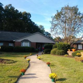 A charming house with a pathway lined by flowers, surrounded by a well-maintained garden and trees.