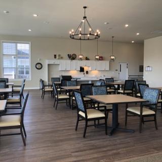 A spacious and modern dining area with multiple tables and chairs, featuring a well-lit kitchen.