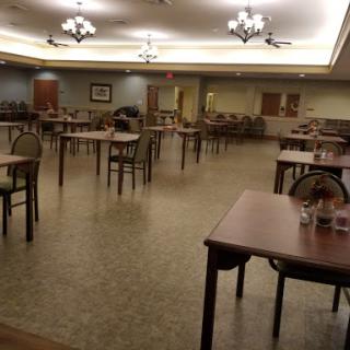 An empty dining room featuring tables and chairs, illuminated by ceiling lights.