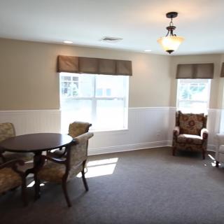 A cozy living room with a table and chairs, featuring large windows and a ceiling light.