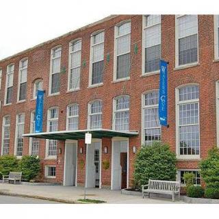 A brick building with large windows and blue banners next to a landscaped entrance.