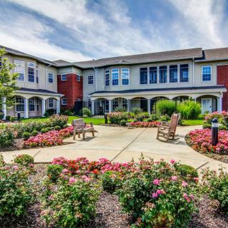 A well-maintained building surrounded by a landscaped garden with benches and colorful flowers under a partly cloudy sky.