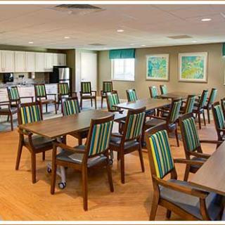 A spacious dining area with multiple tables and chairs, featuring a kitchen area in the background.