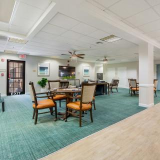 A well-lit dining area with tables and chairs, featuring ceiling fans and a green carpet.