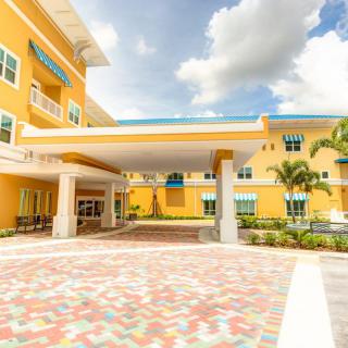 A modern yellow building with a covered entrance and tropical landscaping.