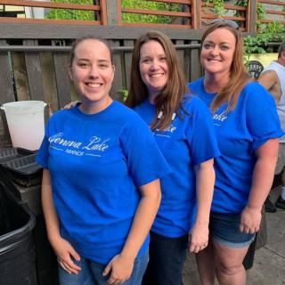 A group of women wearing matching blue shirts, smiling outdoors.