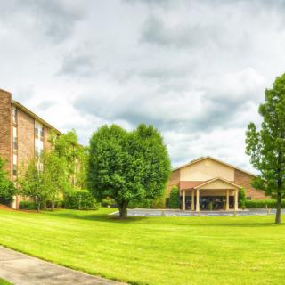 A scenic view of a building surrounded by lush greenery and trees under a cloudy sky.