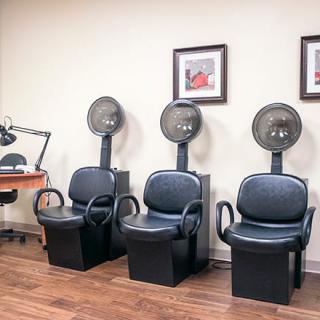 A salon waiting area featuring three hair dryer chairs and framed artwork on the wall.