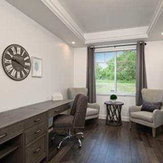 A modern home office with a desk, chairs, and a large window providing natural light.