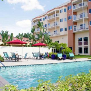 An inviting swimming pool in front of a multi-story apartment building, surrounded by lounge chairs and red umbrellas.