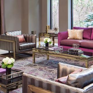 A modern living room with stylish furniture and decor, featuring a purple sofa, armchairs, and a coffee table adorned with flowers.